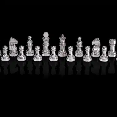 Silberne Schachfiguren des Chess Genius Pro aufgereiht vor schwarzem Hintergrund