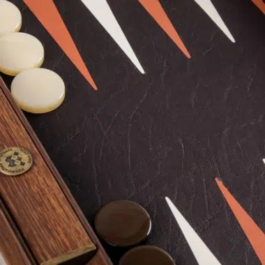 Backgammon aus Leder, elfenbein- und braunfarbene Steine neben graviertem Medaillon