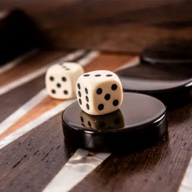 Schwarze Spielsteine und weiße Würfel auf dem mit Perlmuttmotiven verzierten Brett