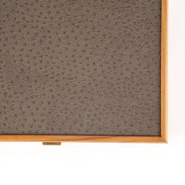 Detail des grauen Straußenleder-Effekts und des goldenen Verschlusses an der Boxecke